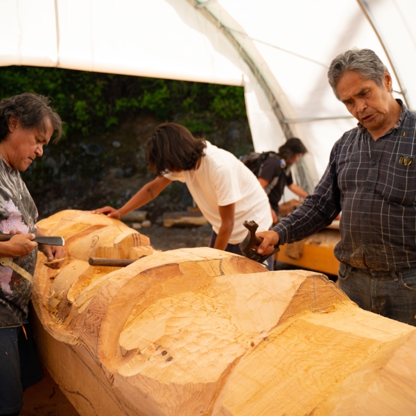 Image gallery pop-up of three individuals working on a large carving from a section of a chopped tree.