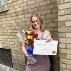 A smiling young woman holding up a degree certificate