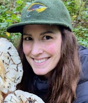 Smiling brown-haired woman wearing a green cap and a blue jacket